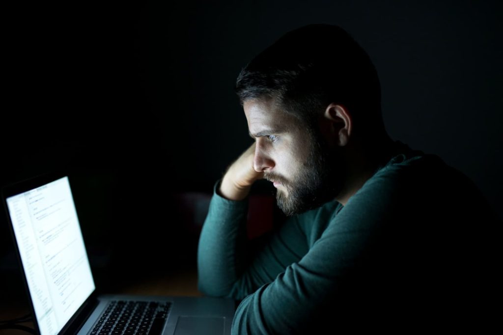 Čovjek sjedi ispred laptopa u mraku, uronjen u digitalni marketing.