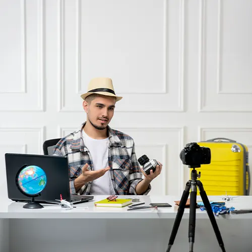 Čovjek sa šeširom sjedi za stolom s prijenosnim računalom i kamerom i radi na brendiranju društvenih medija.